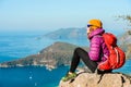 Young woman hiker in bright clothes using digital tablet sit at seaside cliff edge and enjoy the view at mountain peak Royalty Free Stock Photo