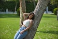 Young woman, Hispanic, beautiful, brunette, with daisy t-shirt and jeans, leaning on a tree trunk, calm and relaxed. Concept of Royalty Free Stock Photo