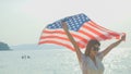 young women hold American flags on the beach and the sea on their summer vacation and they smile and enjoy their vacation Royalty Free Stock Photo