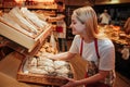 Young woman hold bakset with fresh bread in grocery store. She put it on shelf and smile. Tasty and delisious. Working Royalty Free Stock Photo