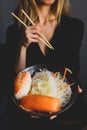 Young woman hold bowl in her hands full of funchose and sushi with salmon and srhrimp.