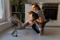 Young woman holding beloved cat sits in front of electric fan and relaxes at blower cold air stream