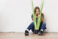 Young woman holding big green plant sitting against wall. Royalty Free Stock Photo