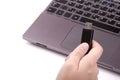 Young woman holding a black USB flash drive in her hand, with a defocused silver laptop with a keyboard in the background. Royalty Free Stock Photo