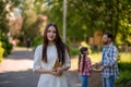 Young Woman Is Holding The Book While Standing In The Park.Her Hasband And Daughter Holding Each Other Hands And Making