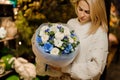 Young woman holding a bouquet with blue and white flowers wrapped in matte transparent paper decorated with green leaves Royalty Free Stock Photo