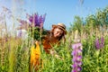 Young woman holding bouquet of lupin flowers walking in summer meadow. Stylish girl picking purple blooms Royalty Free Stock Photo