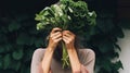 Young woman holding a bunch of fresh leafy greens in front of her face. Healthy plant base diet vitamins veganism concept