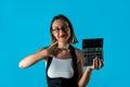 Young woman holding calculator and smiling or wondering isolated on blue background. Royalty Free Stock Photo