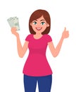 Young woman holding cash/currency/money in hand and showing thumbs up sign. Deal, agree, approve, success, business and finance. Royalty Free Stock Photo