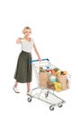 young woman holding credit card and looking at camera while standing with shopping trolley full of grocery Royalty Free Stock Photo