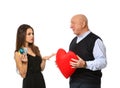 Young woman holding credit cards and senior man with red heart on white background. Marriage of convenience Royalty Free Stock Photo