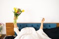 Happy young Asian woman wearing pajamas holding cup and tulips flowers on the bed having fun Royalty Free Stock Photo