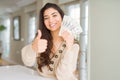 Young woman holding 20 dollars bank notes happy with big smile doing ok sign, thumb up with fingers, excellent sign Royalty Free Stock Photo