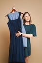 Young woman holding dresses on hanger, trying to decide what to wear.