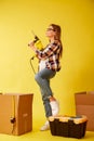 Young woman holding a drill, standing between the boxes for moving. Studio