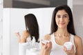 Young Woman Holding Face Cream Product Standing In Bathroom