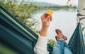 Young woman holding in fingers and examining small yellow birch tree leaf as she swinging in hammock on the mountain lake bank. Royalty Free Stock Photo