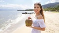 Young woman holding a fresh coconut enjoying on tropical beach. Healthy girl relaxing on the beach in her holiday holding a green Royalty Free Stock Photo