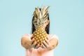 Young woman is holding a fresh and delicious pineapple and posing isn studio front of a blue font isolated.