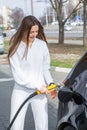 Young woman holding a fuel nozzle in her hand while refueling car at gas station.