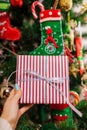 Young woman holding gift box in front of Christmas tree at home. New year present. Closeup Royalty Free Stock Photo