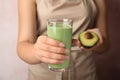 Young woman holding glass of tasty avocado smoothie on light background