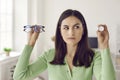 Young woman holding glasses and eye lenses and hesitating which solution to choose