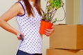 Young woman holding green plant and grabbing suitcase handle with the other, boxes stacked background, moving in concept Royalty Free Stock Photo