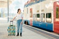 Young woman holding her luggage and waiting departure. Train station is in background. Colorful train in background Royalty Free Stock Photo