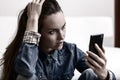 Young woman holding his head and looks to the smartphone. Distressed by what he saw