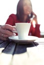 Young woman holding a hot cup of coffee while talking with her mobile phone sitting in the terrace of coffe shop Royalty Free Stock Photo