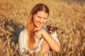 Young woman holding Jack Russell terrier puppy on her hands, both of them smiling, sunset lit wheat field in background Royalty Free Stock Photo