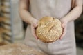 Young woman holding loaf of fresh whole wheat bread in bakery