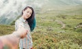 Young woman holding male hand and leading him in summer mountains.