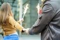 Young woman holding man with fireworks in hands during city festival - Boyfriend following beloved girlfriend in winter holidays