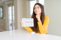 Young woman holding menstruation calendar serious face thinking about question, very confused idea