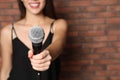 Young woman holding microphone near brick wall