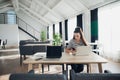 Young woman holding mobile phone and typing SMS while sitting at wooden table with open laptop computer. Royalty Free Stock Photo