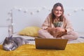 Young woman is holding money while sitting on the bed with a cat. Girl with dollars in hands in home bedroom, work online