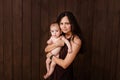 Young woman holding a newborn baby in her arms on the brown background. Newborn photosession. Family portrait. Mother is kissing