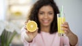 Young woman holding out orange and glass of juice and smiling, rich in vitamins