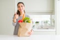 Young woman holding paper bag full of groceries happy with big smile doing ok sign, thumb up with fingers, excellent sign Royalty Free Stock Photo