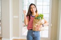 Young woman holding paper bag full of groceries very happy pointing with hand and finger to the side Royalty Free Stock Photo