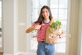 Young woman holding paper bag full of groceries very happy pointing with hand and finger Royalty Free Stock Photo
