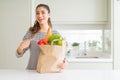 Young woman holding paper bag full of groceries very happy pointing with hand and finger Royalty Free Stock Photo