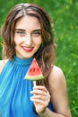 Young woman is holding piece of watermelon like ice cream on a green nature background