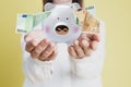 Woman holding piggy bank and Euro banknotes falling on color background, closeup Royalty Free Stock Photo