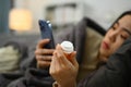 Young woman holding pill bottle checking prescription medicine on smartphone. Telemedicine and healthcare concept. Royalty Free Stock Photo