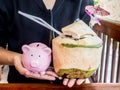 Young woman holding Pink piggy bank with coconut drink, savings money for spending in holidays and retirement fund concept